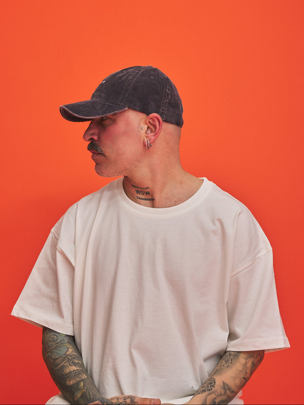 Person wearing a white t-shirt and charcoal grey cap against an orange background