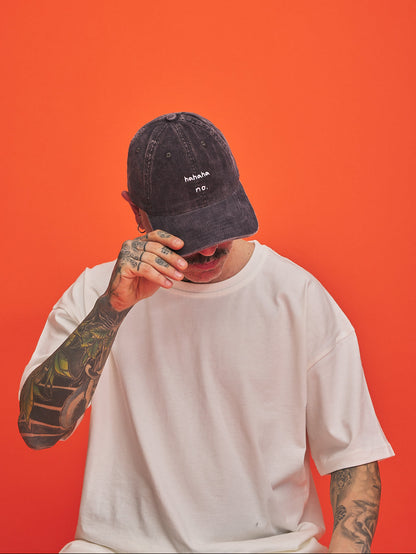 Person wearing a charcoal grey corduroy cap and white t-shirt against an orange background