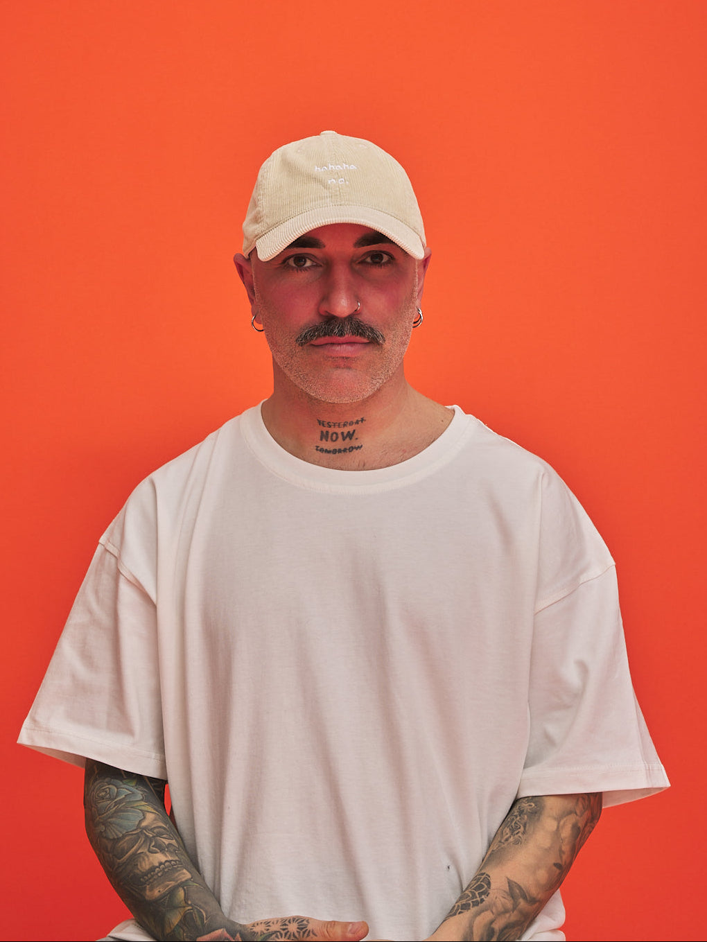 Man wearing Beige cream corduroy cap and white t-shirt against an orange background