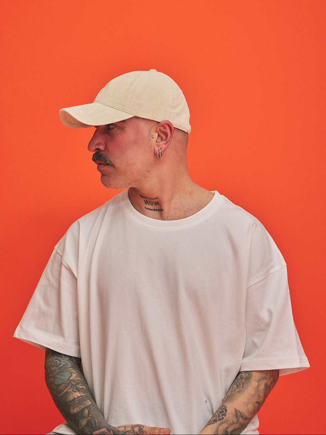 Man wearing Beige cream corduroy cap and white t-shirt against an orange background