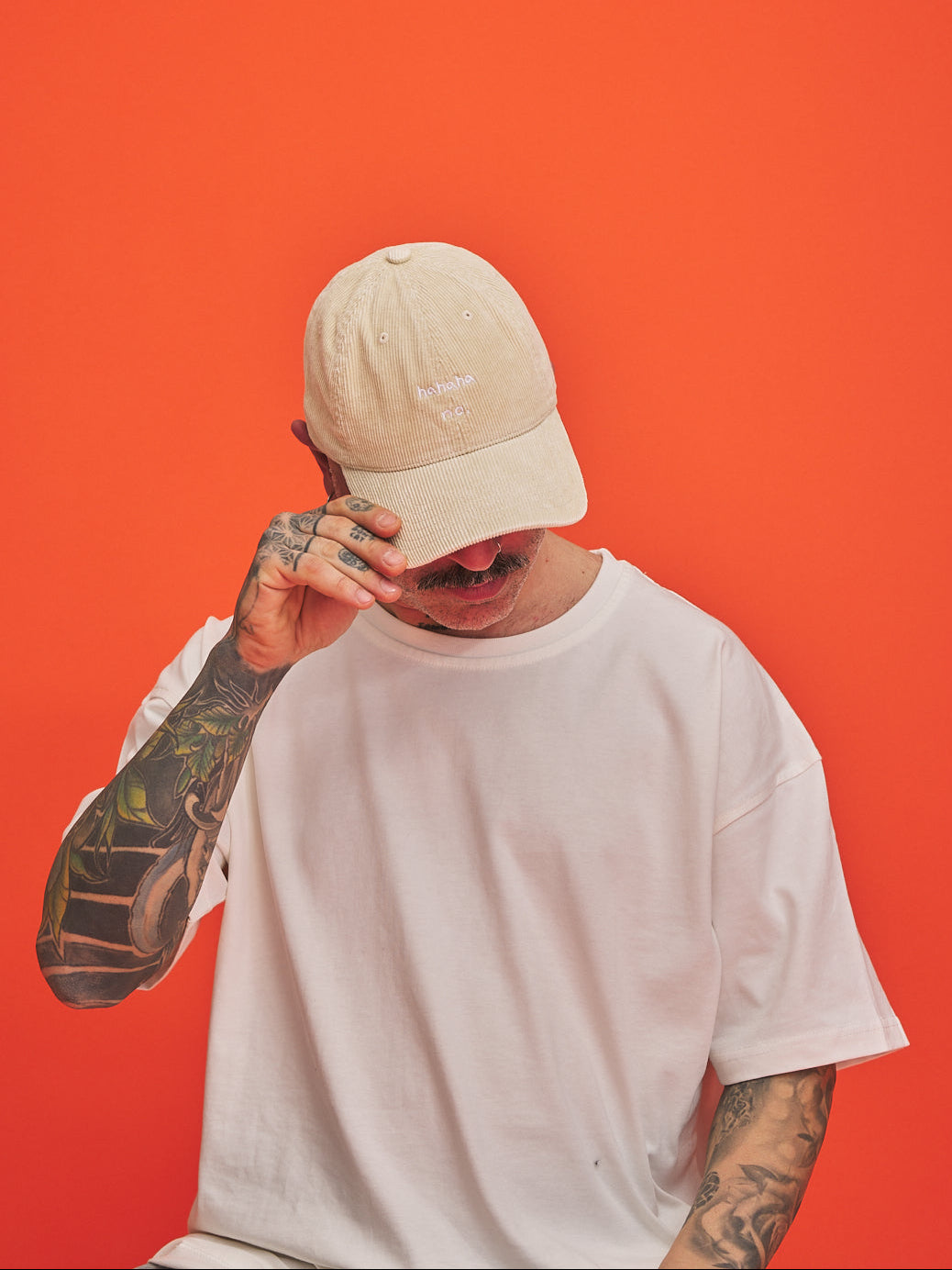 Person wearing a Beige cream corduroy cap and white t-shirt against an orange background