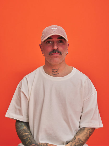 Man wearing a white t-shirt and pink cap against an orange background
