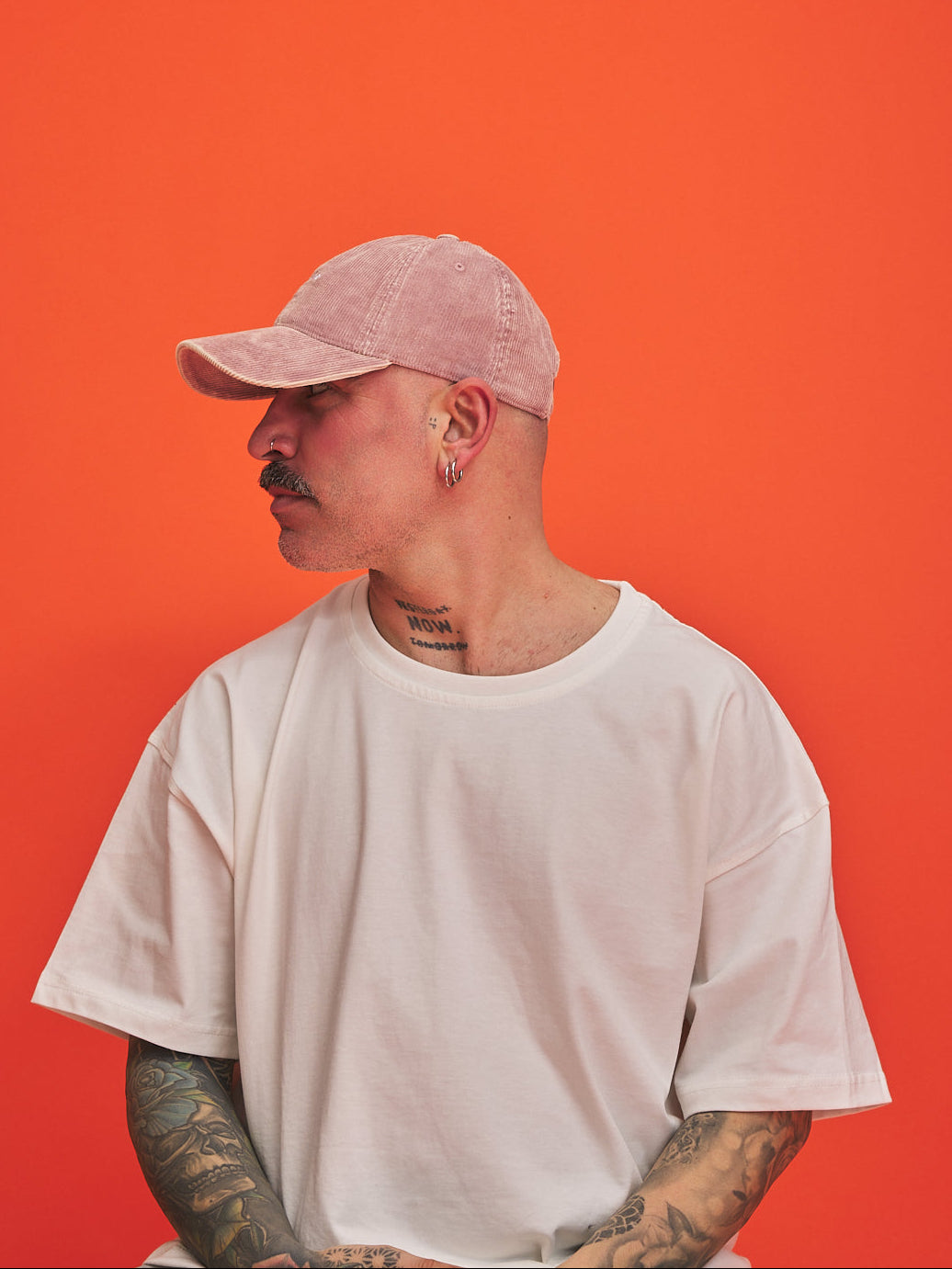 Person wearing a light pink cap and white t-shirt against an orange background