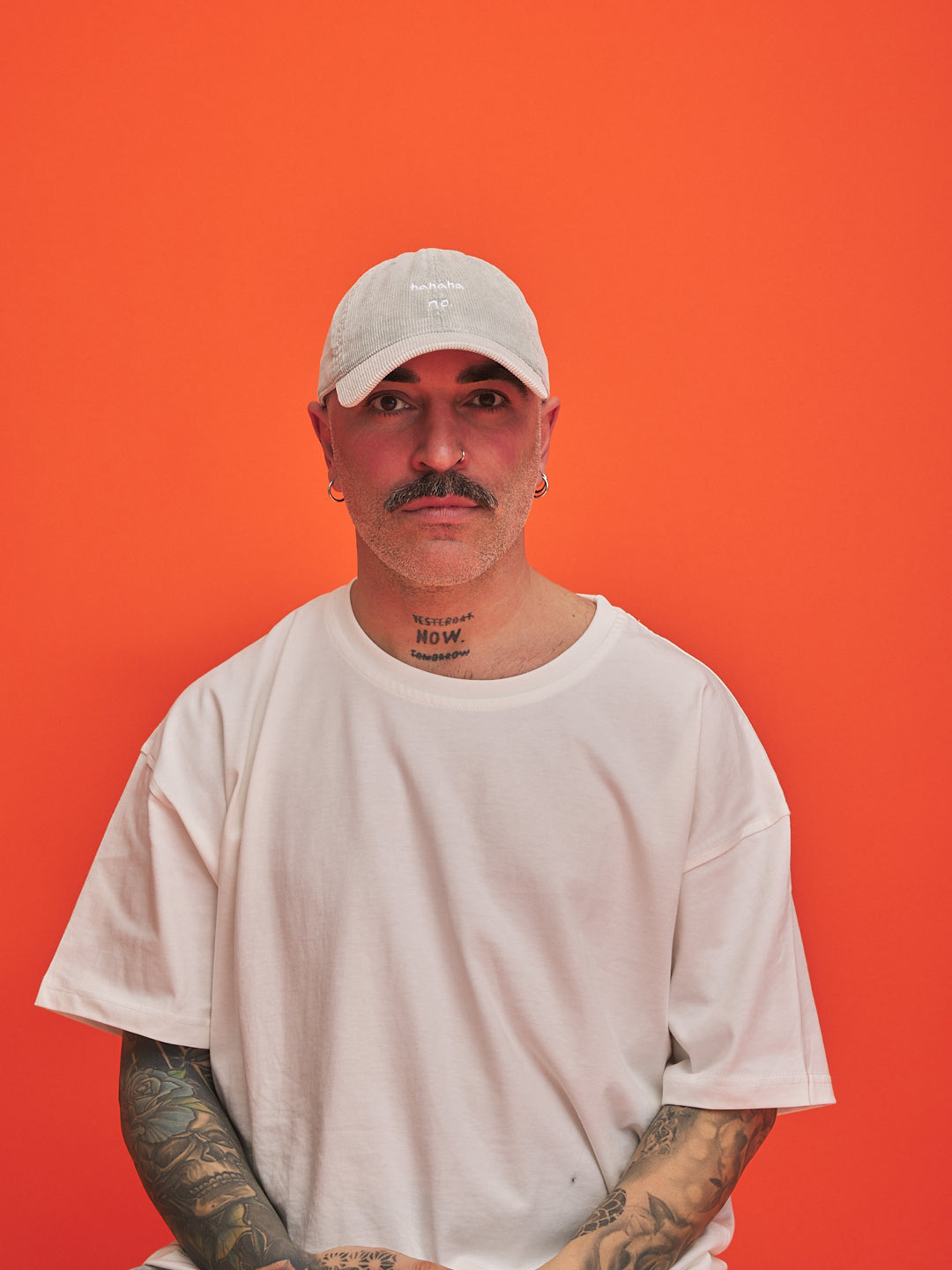 Man wearing Hahaha No Light Grey Corduroy Cap and white t-shirt against an orange background