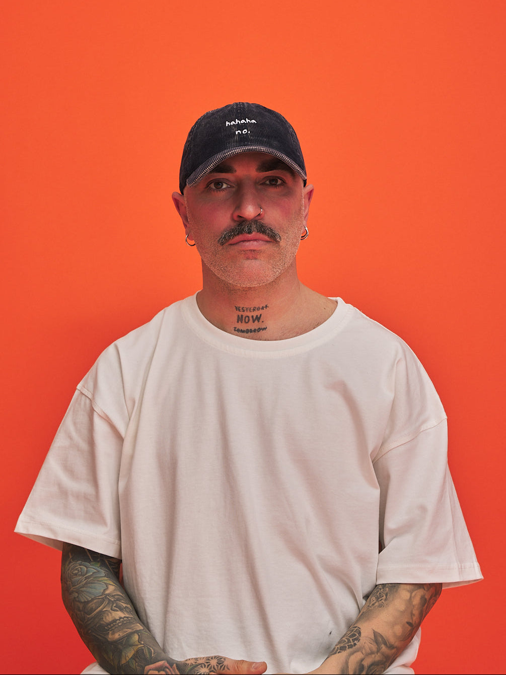 Man wearing a navy blue corduroy cap and white t-shirt against an orange background