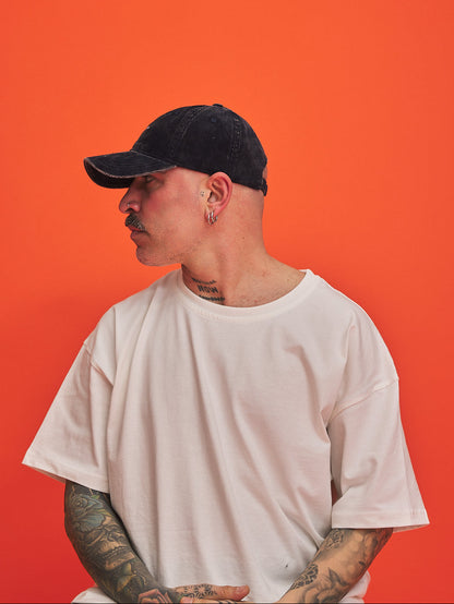 Person wearing a navy blue corduroy cap and white t-shirt against an orange background