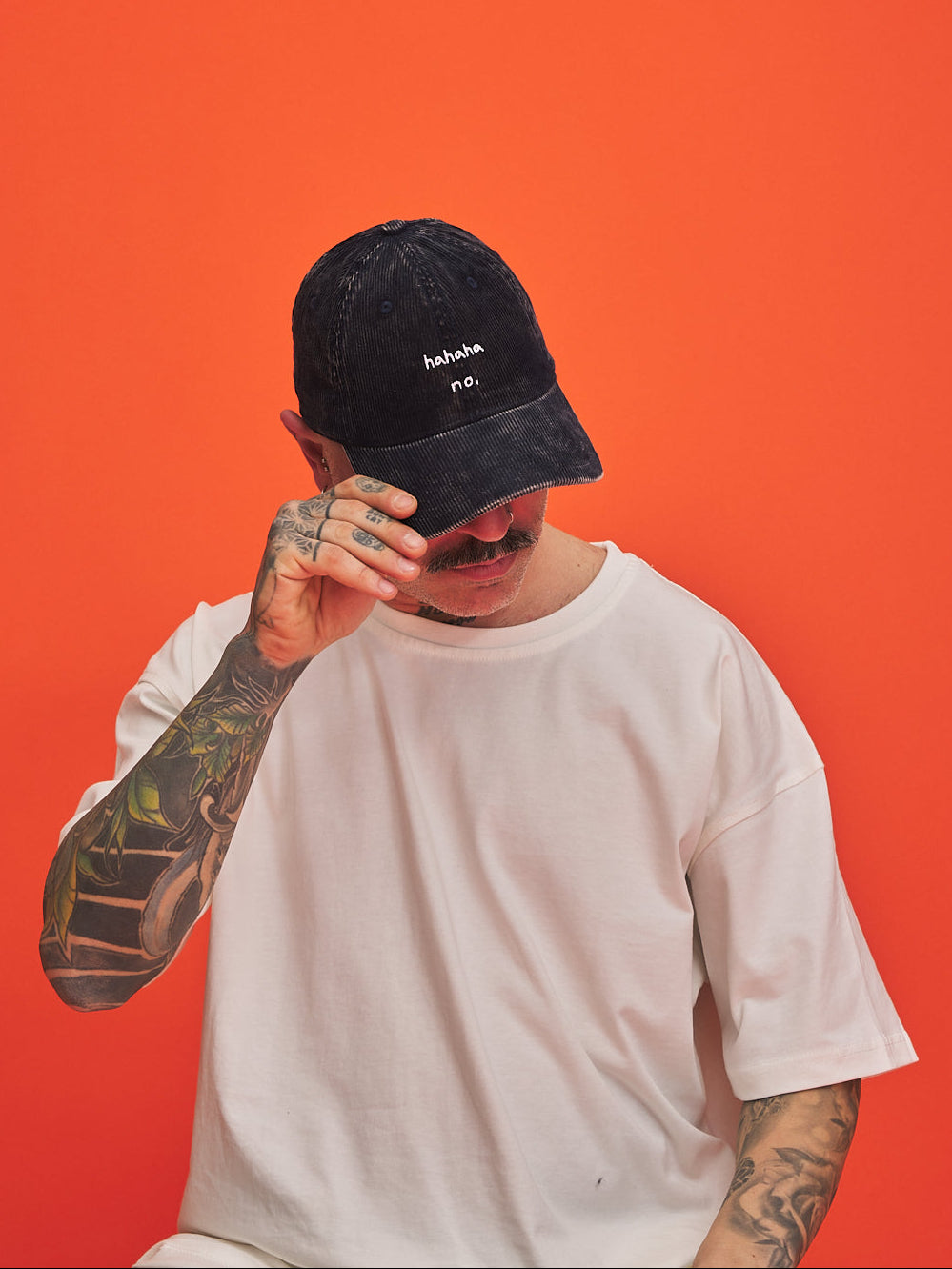 Person wearing a navy blue corduroy cap and white t-shirt against an orange background