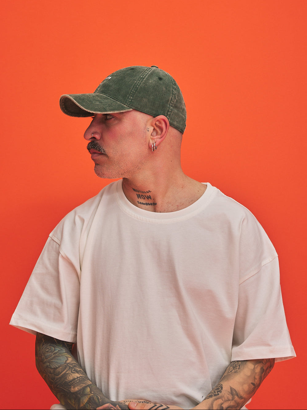 Man wearing a green cap and white t-shirt against an orange background