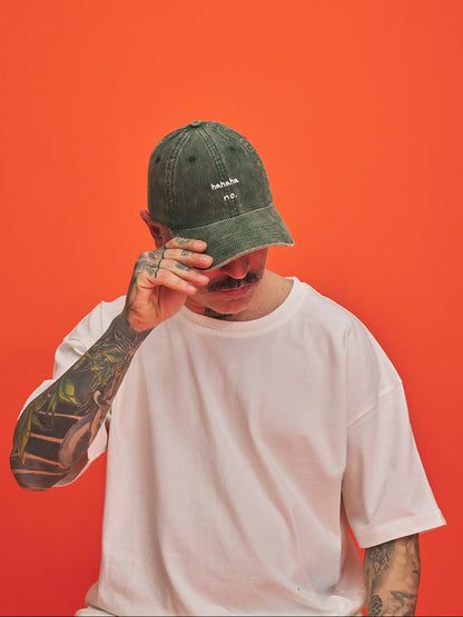 Person wearing a olive green corduroy cap and white t-shirt against an orange background