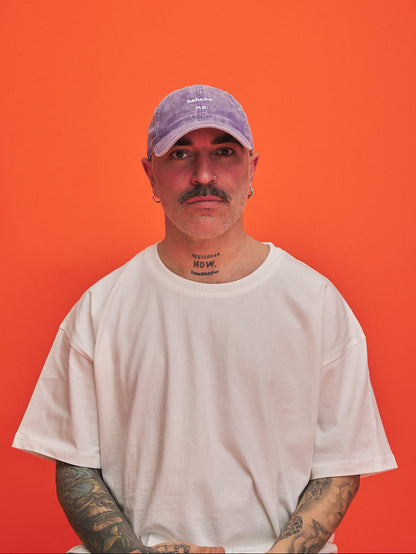 Man wearing a white t-shirt and purple corduroy cap against an orange background