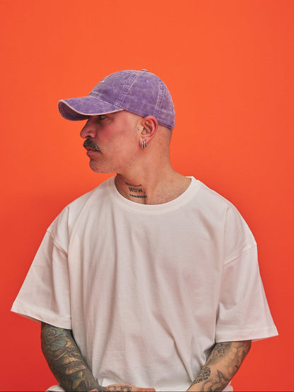 Person wearing a white t-shirt and purple corduroy cap against an orange background