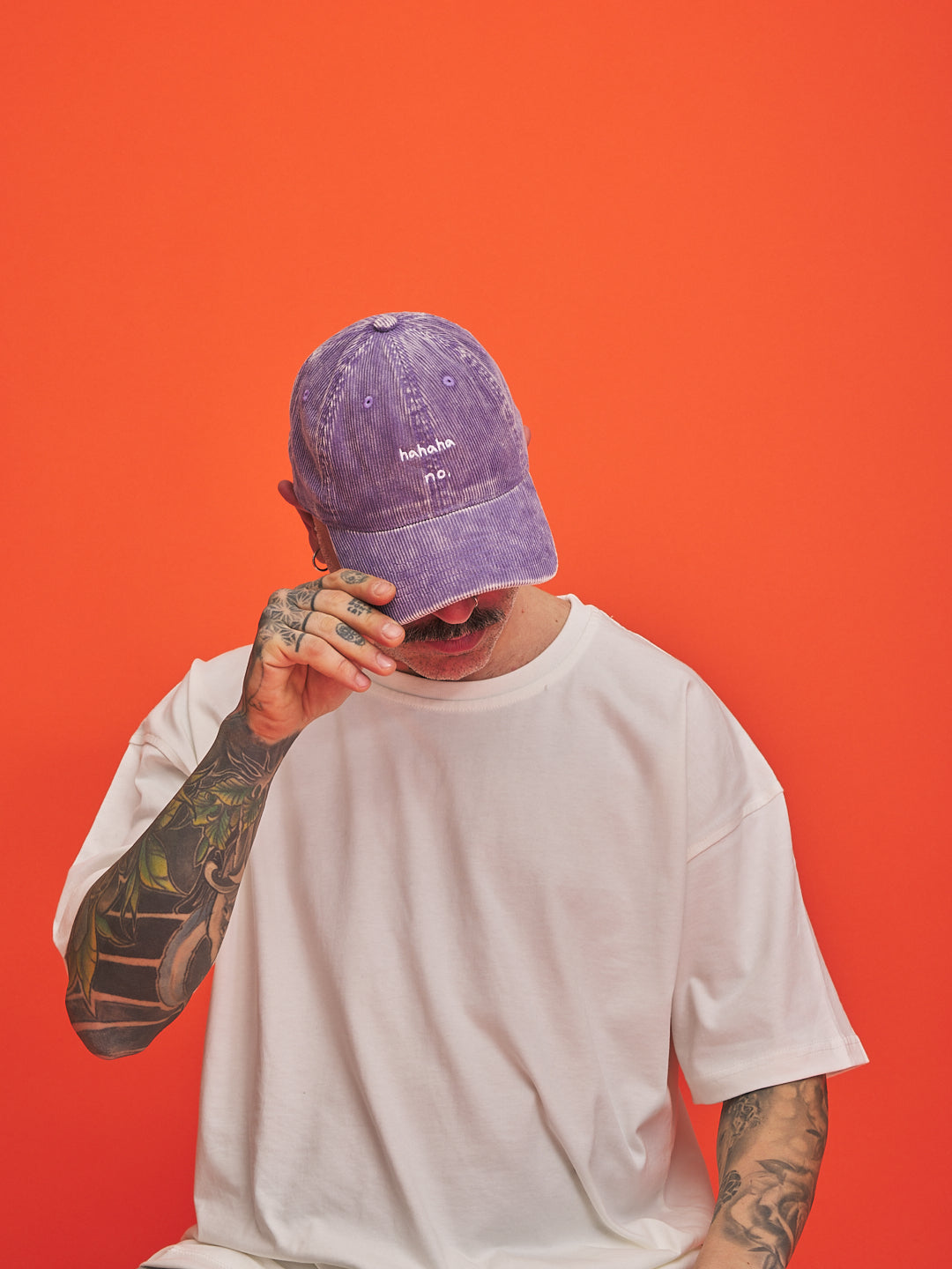 Person wearing a purple corduroy cap and white t-shirt against an orange background
