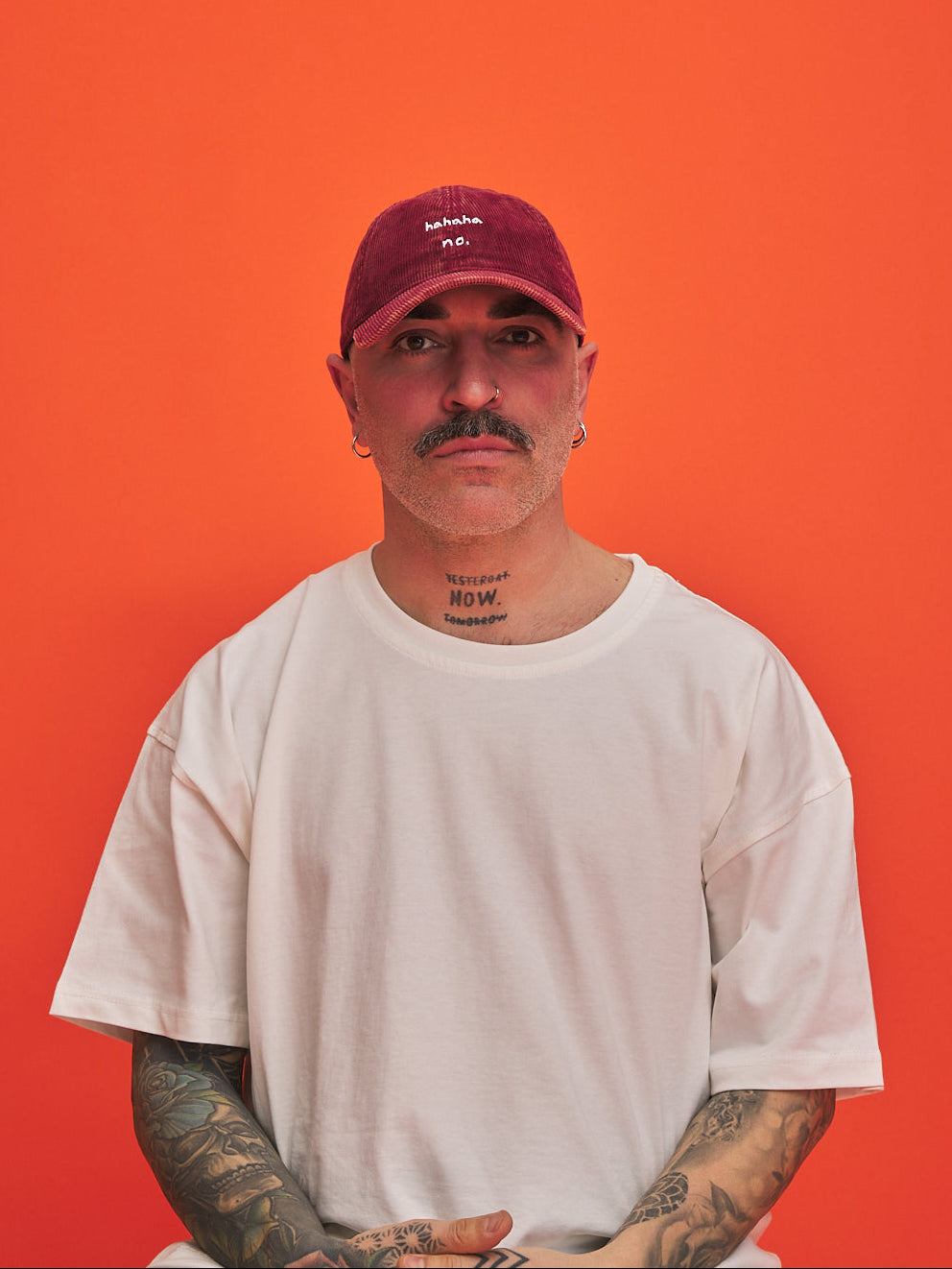 Man wearing a white t-shirt and red corduroy cap against an orange background