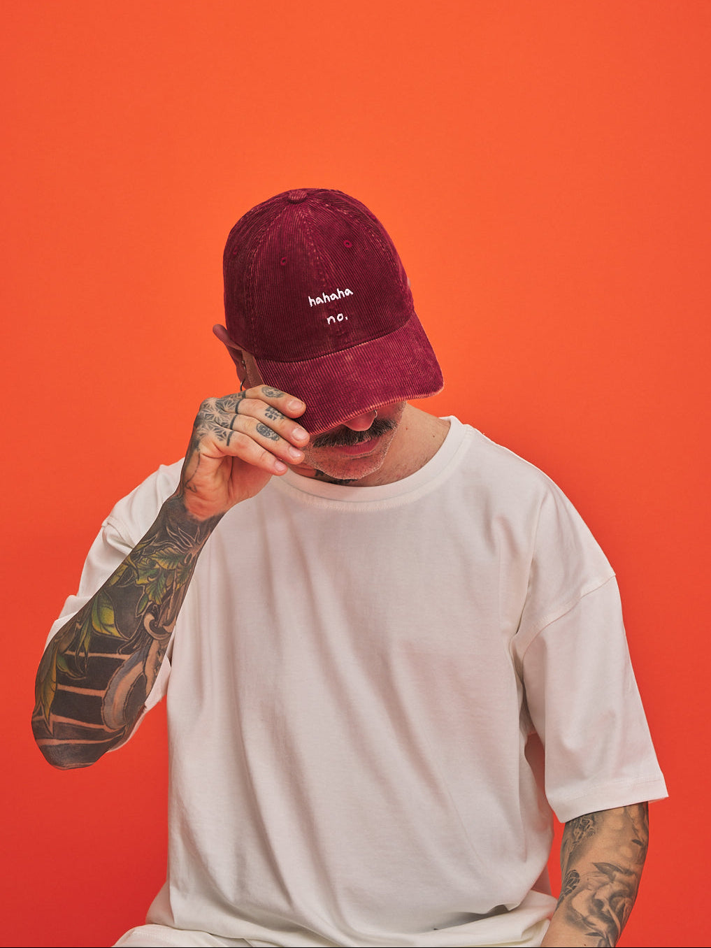 Person wearing a Hahaha No Red Corduroy Cap with text on an orange background