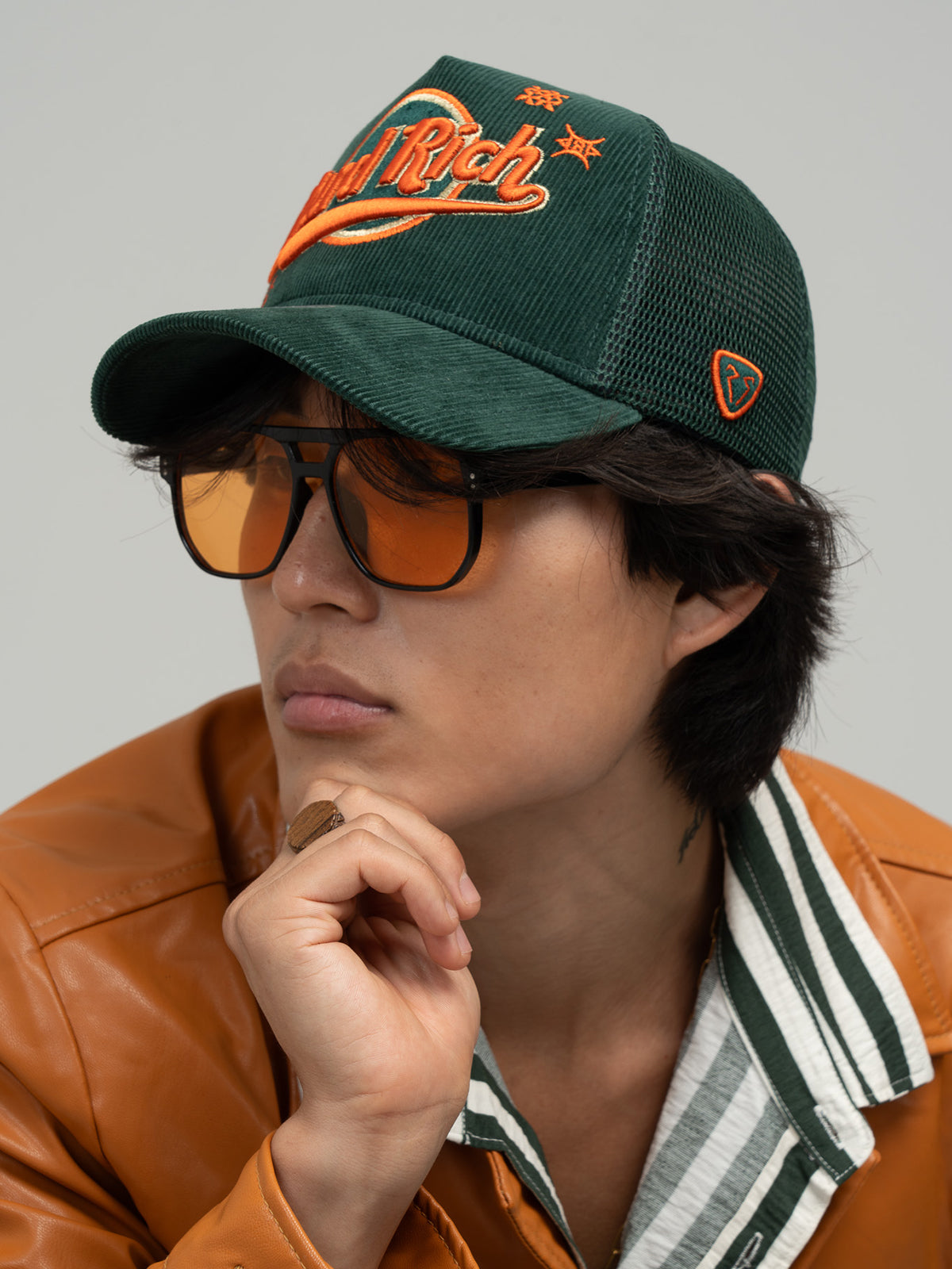 Person wearing Hard Rich Green Trucker Hat, sunglasses, and a brown leather jacket.