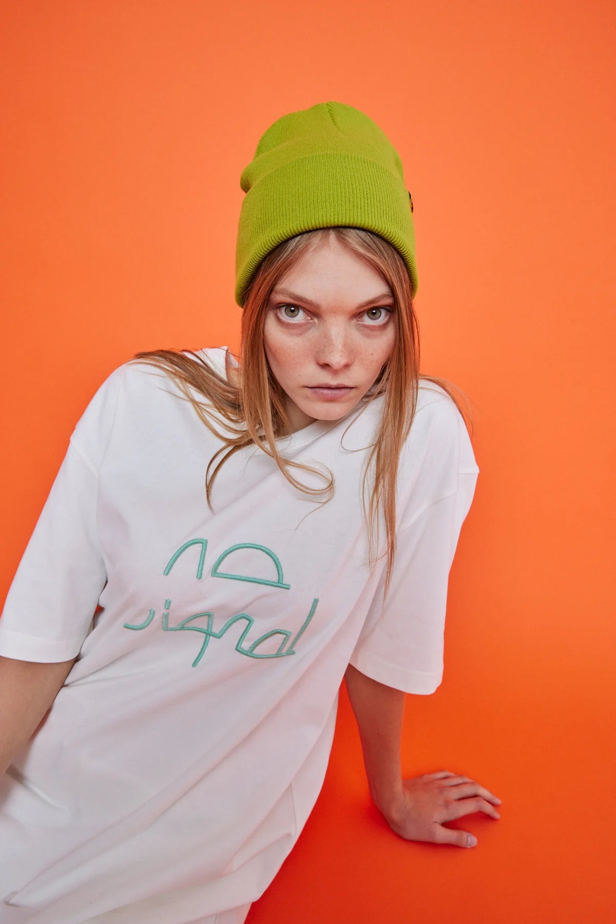 Person wearing a white t-shirt with green text and a green beanie against an orange background