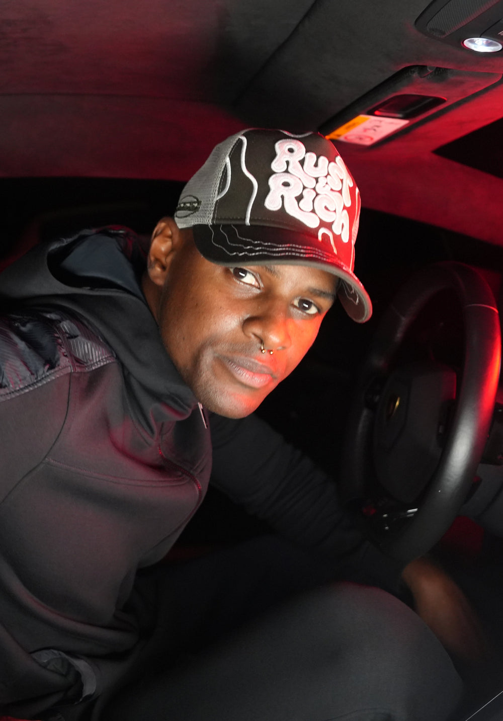Person wearing Rust & Rich Gray Trucker Hat inside a vehicle with red interior lighting