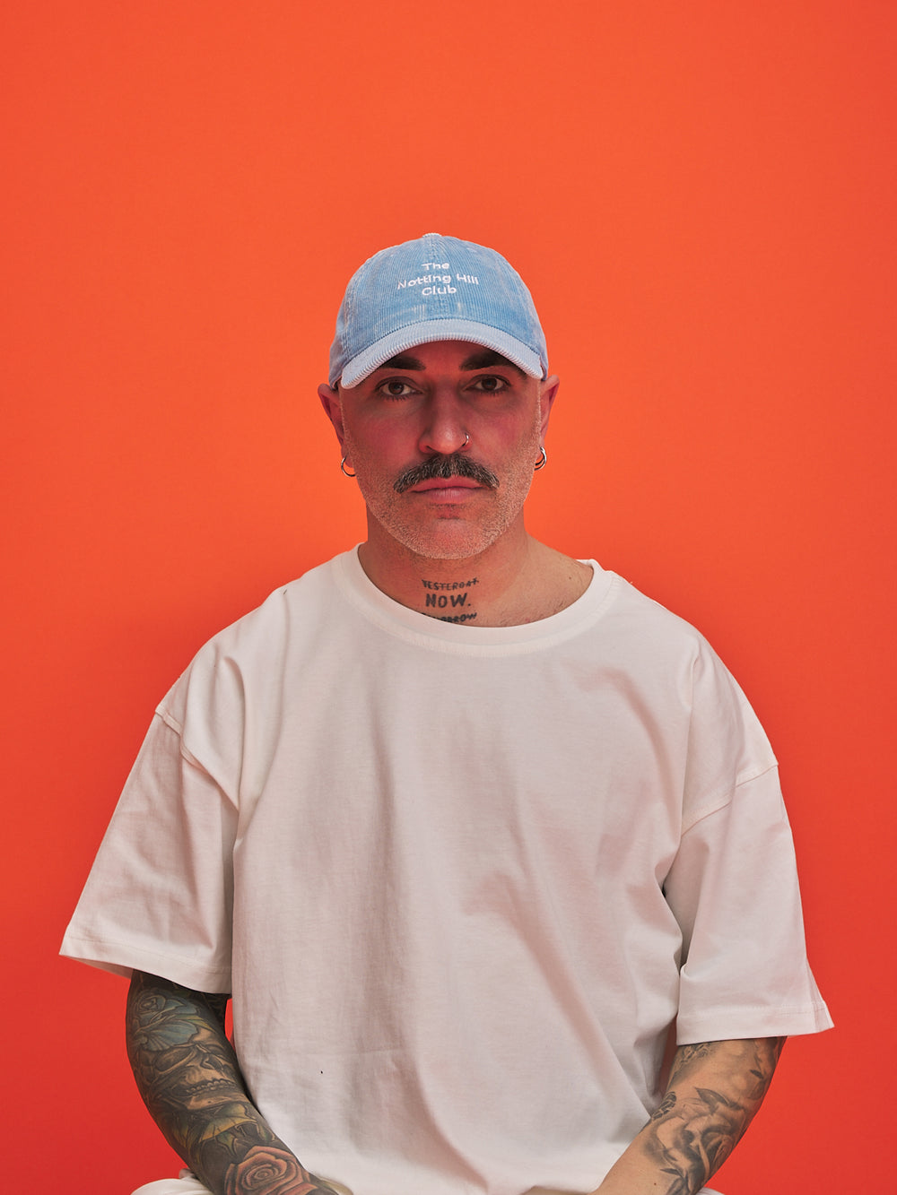 Man wearing a light blue cap and white t-shirt against an orange background