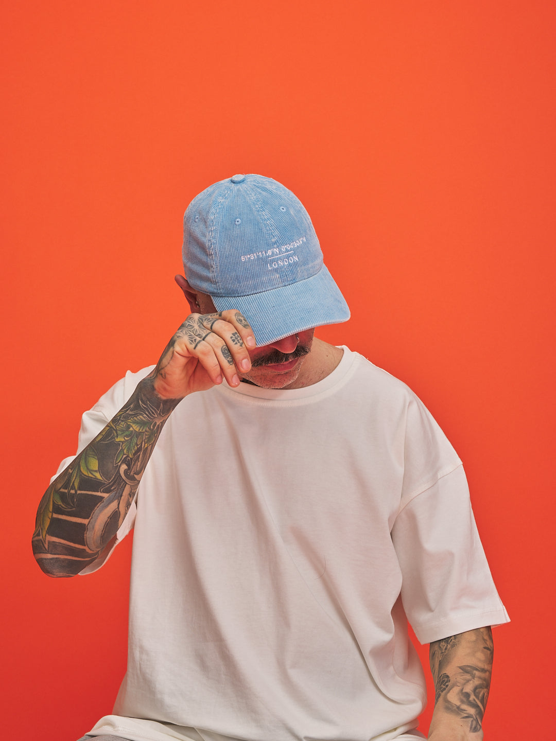 Person wearing a blue cap and white t-shirt against an orange background