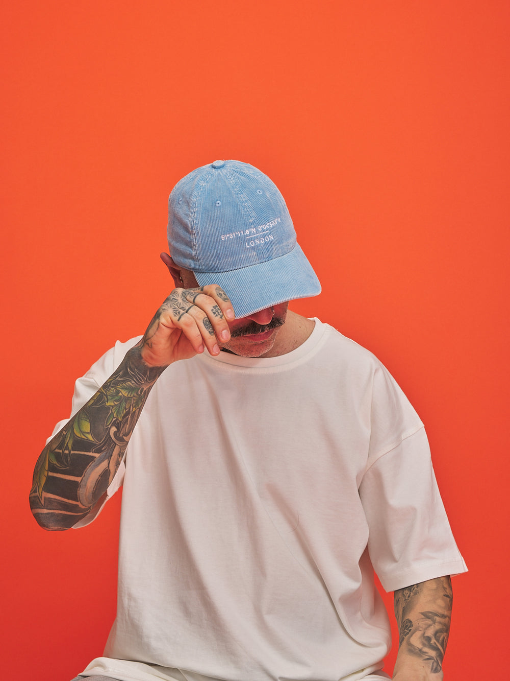 Person wearing a blue cap and white t-shirt against an orange background