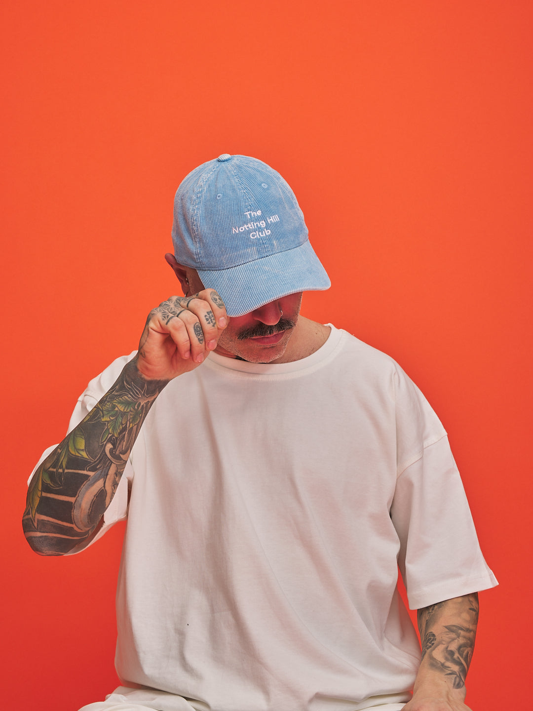 Person wearing a blue cap and white t-shirt against an orange background