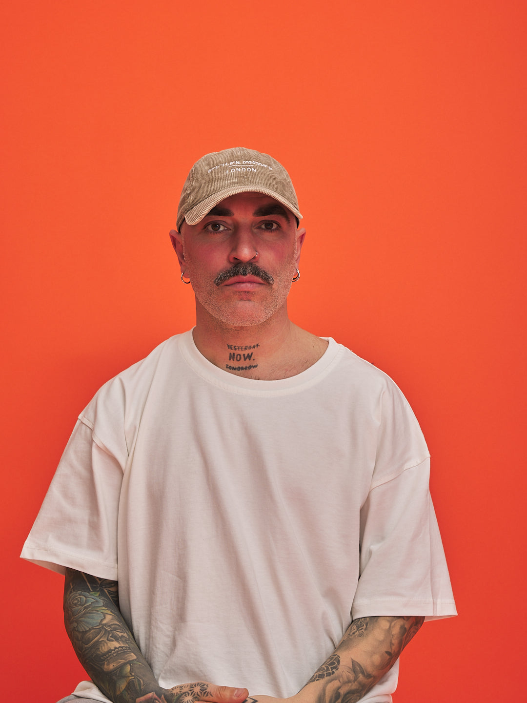 Man wearing a beige cap and white t-shirt against an orange background