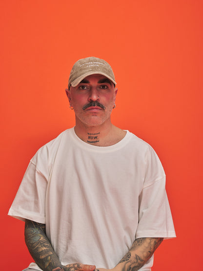 Man wearing a beige cap and white t-shirt against an orange background