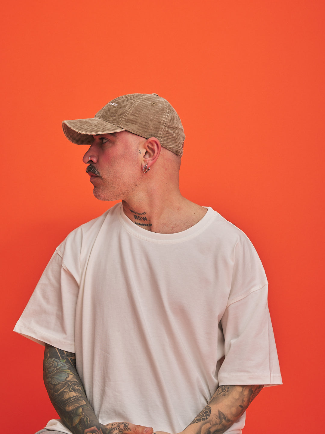 Person wearing a beige cap and white t-shirt against an orange background