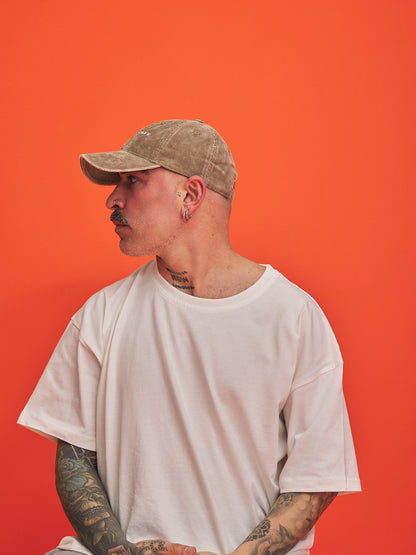 Person wearing a beige cap and white t-shirt against an orange background