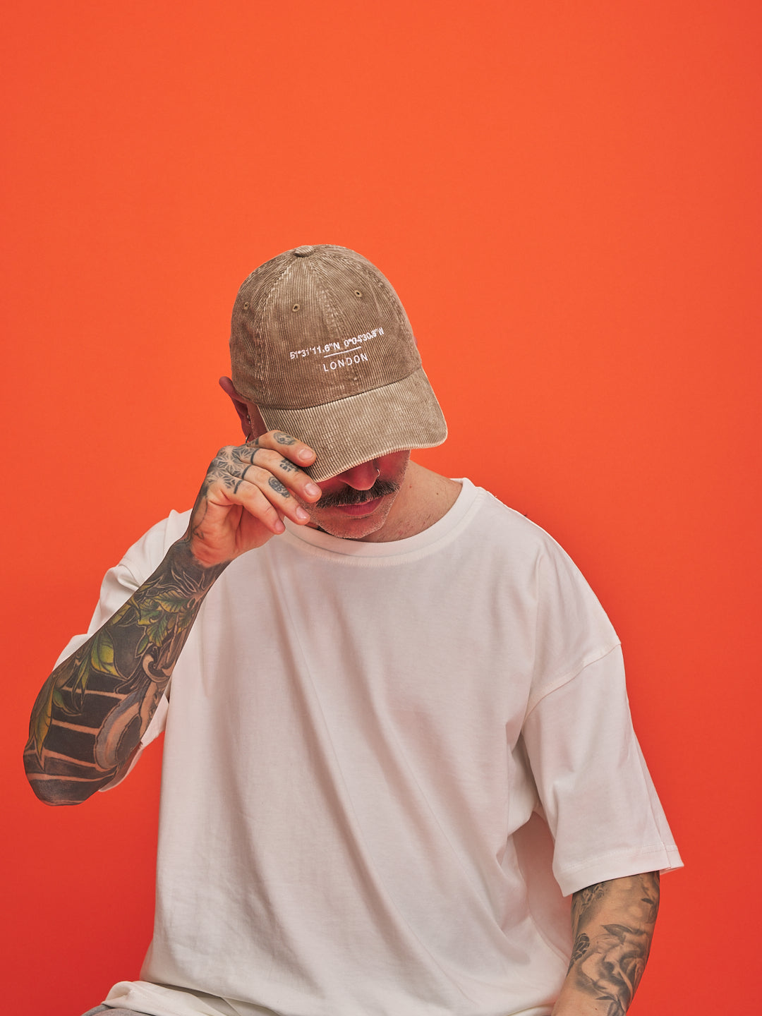 Person wearing a cap and white t-shirt against an orange background