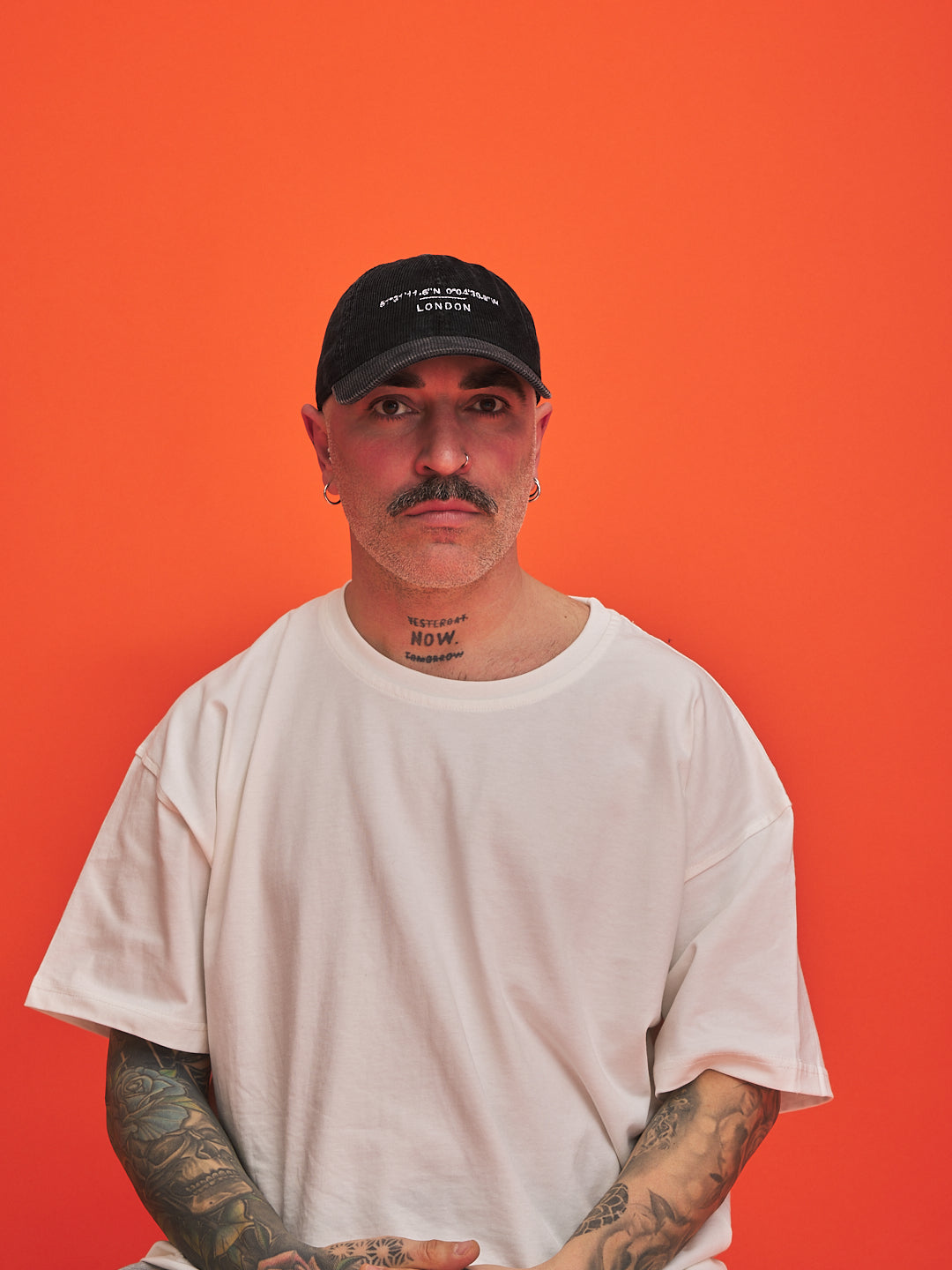 Man wearing a black cap and white t-shirt against an orange background