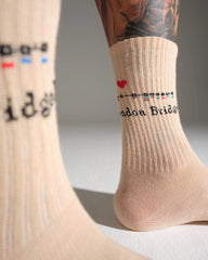 Beige London Bridge location and text socks with a heart design worn by a person with tattoos.