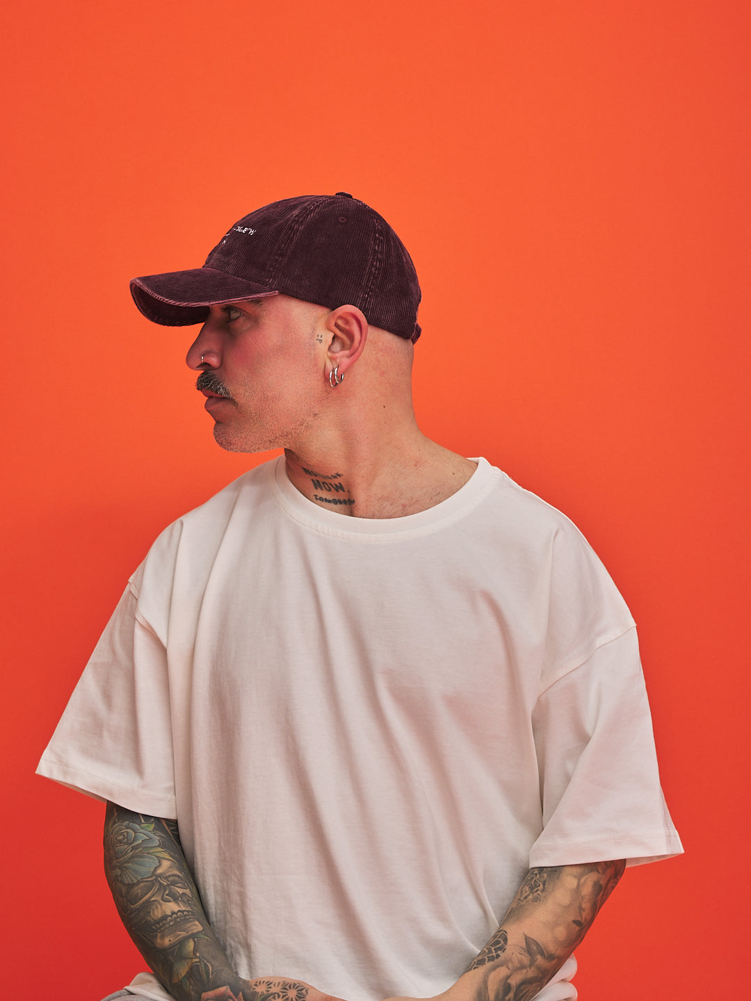 Person wearing a white t-shirt and dark cap against an orange background