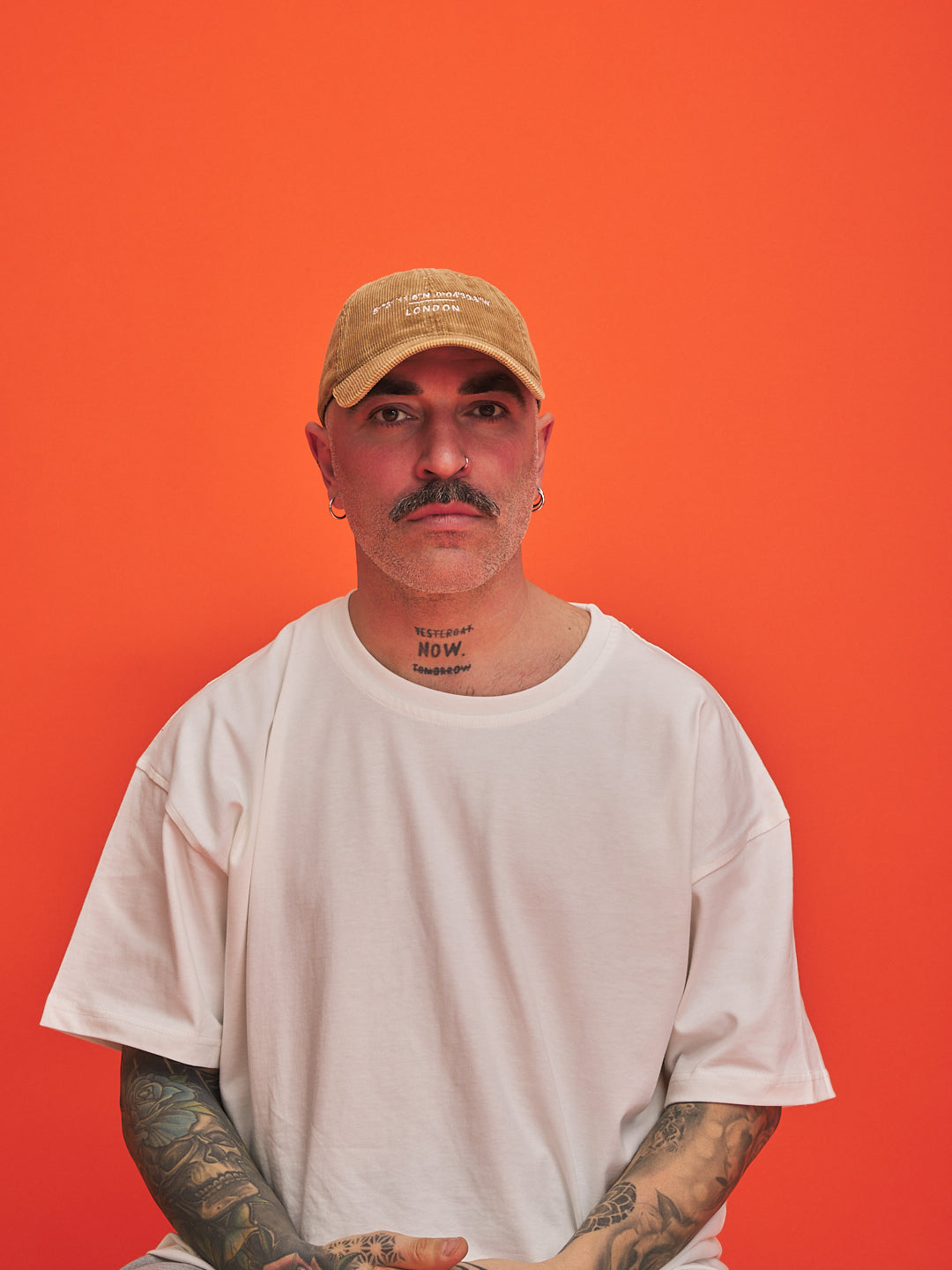 Man wearing a camel cap and white t-shirt against an orange background