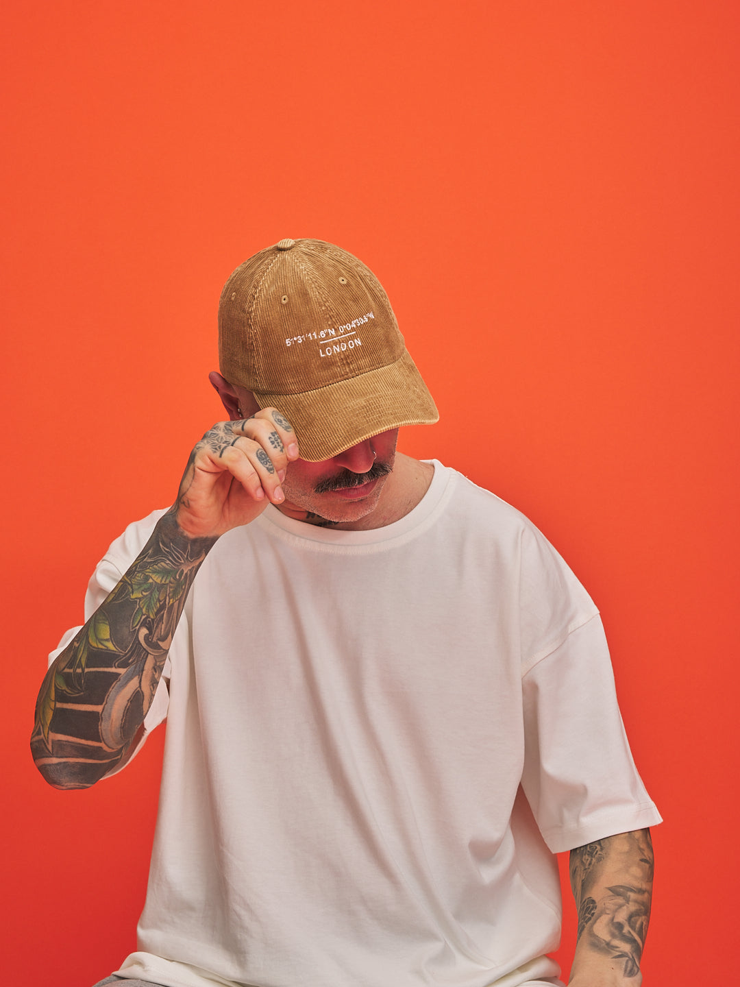 Person wearing a camel cap and white t-shirt against an orange background