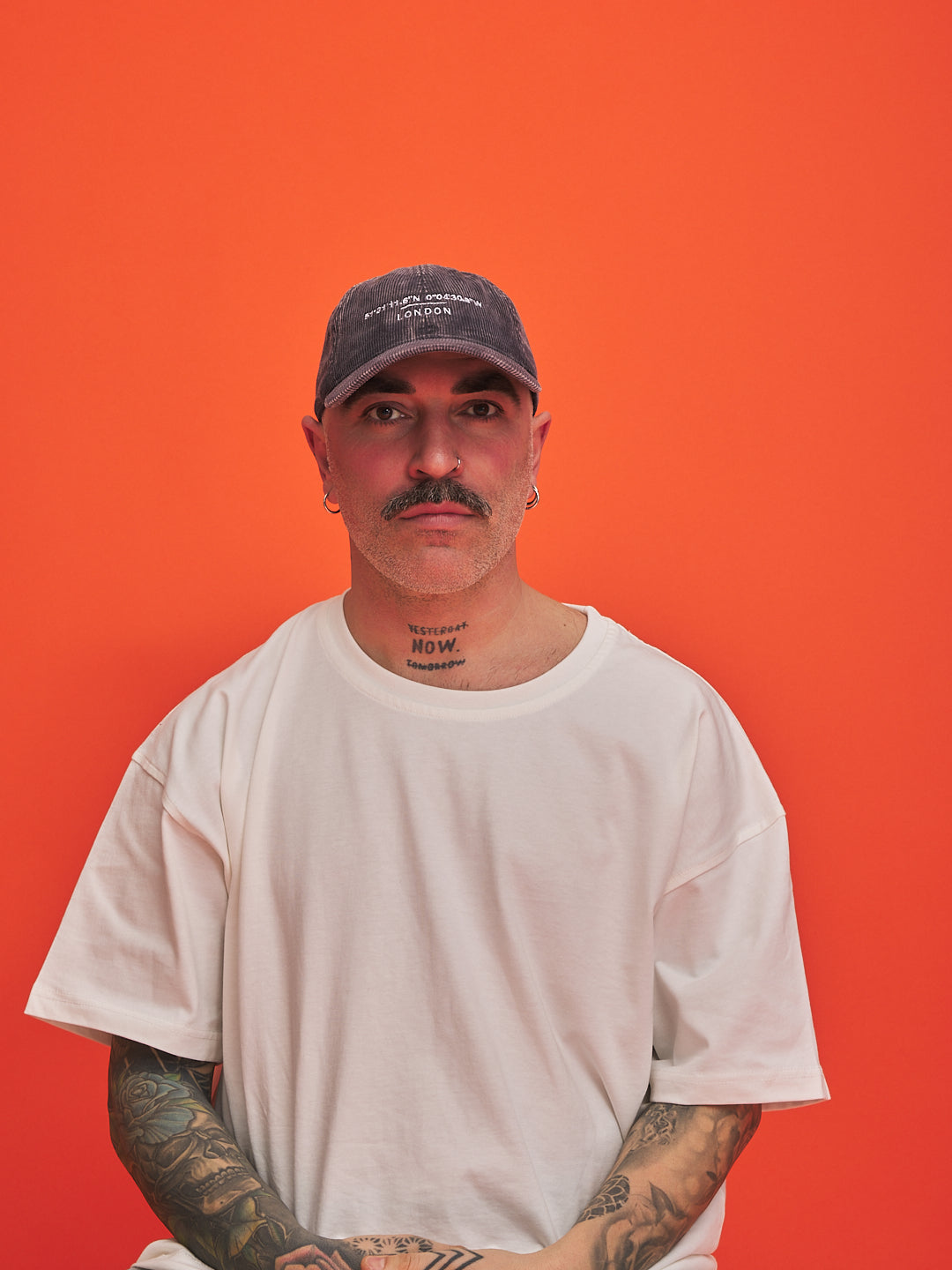 Person wearing a cap and white t-shirt against an orange background