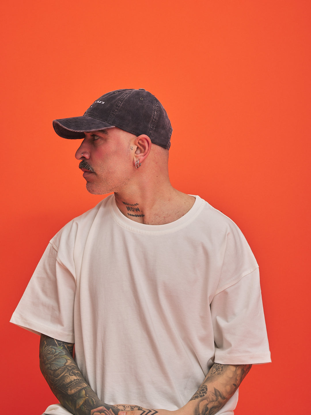 Person wearing a white t-shirt and dark cap against an orange background