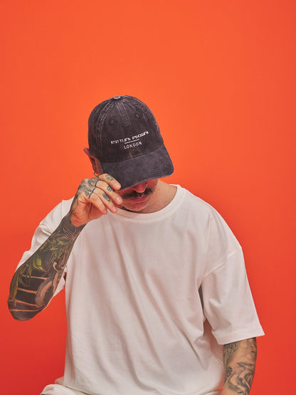 Person wearing a charcoal grey cap and white t-shirt against an orange background