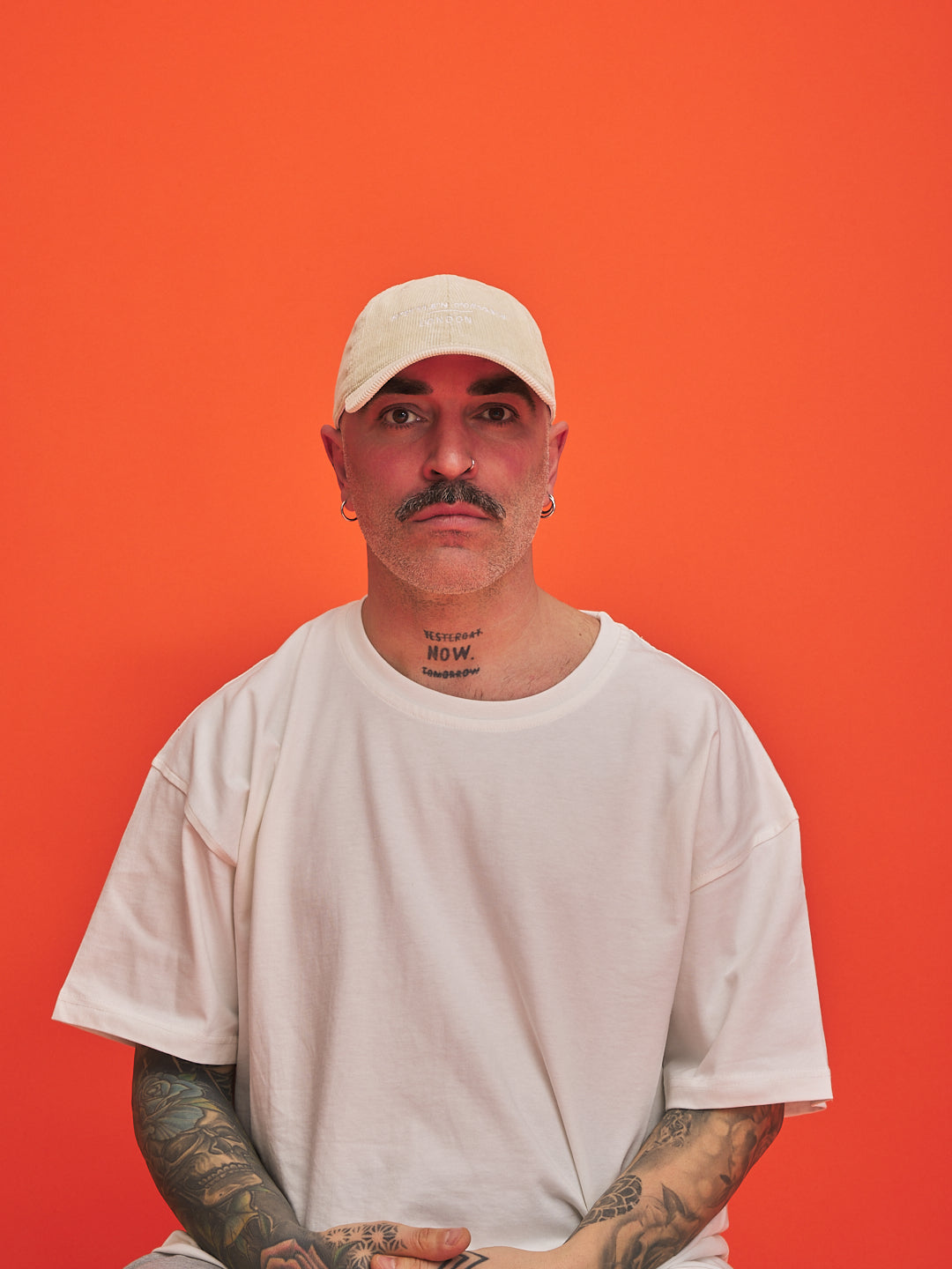 Man wearing a cream cap and t-shirt against an orange background