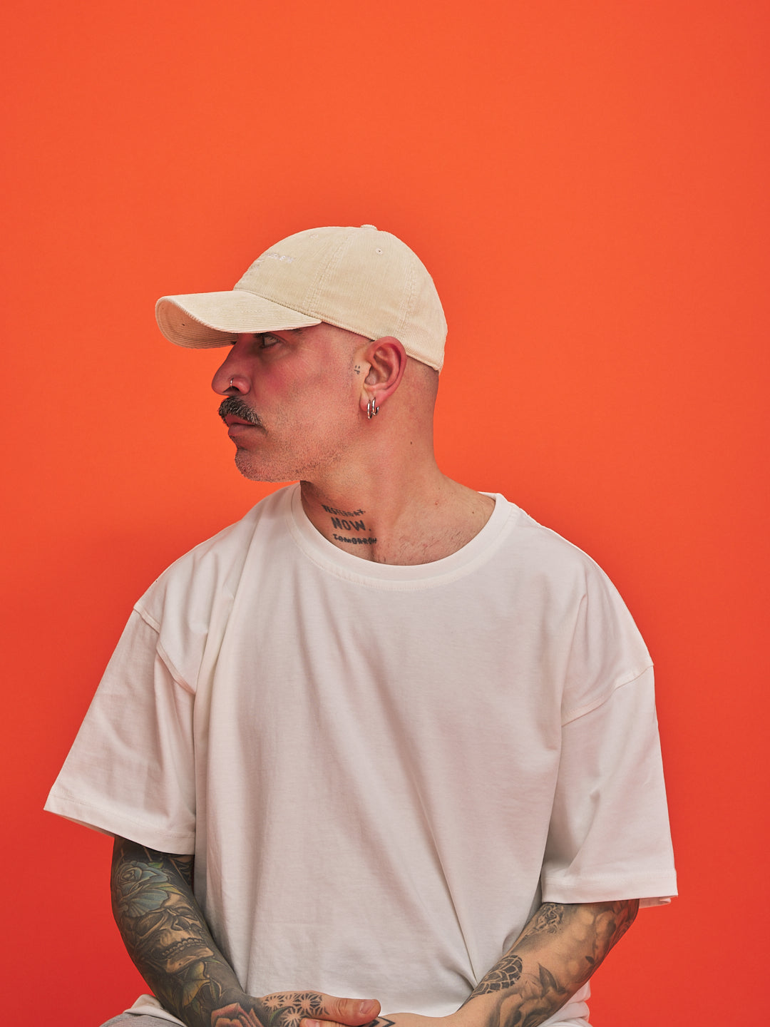 Man wearing a cream cap and white t-shirt against an orange background