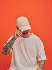 Man wearing a cream cap and white t-shirt against an orange background