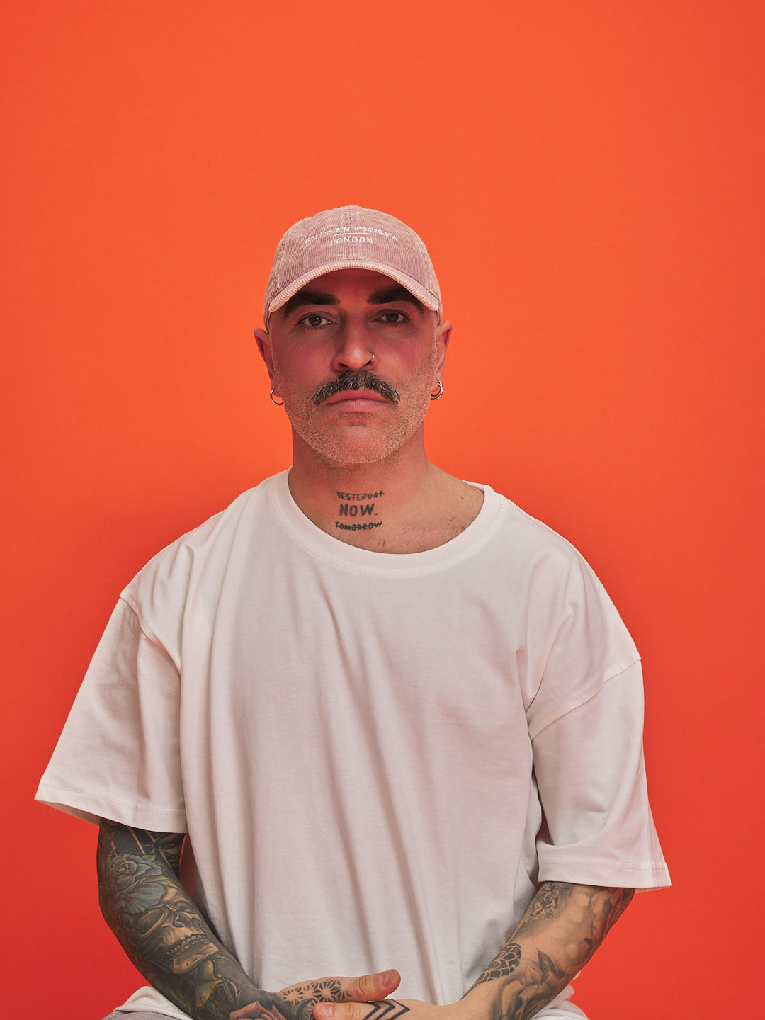 Man wearing a light-colored cap and t-shirt against an orange background