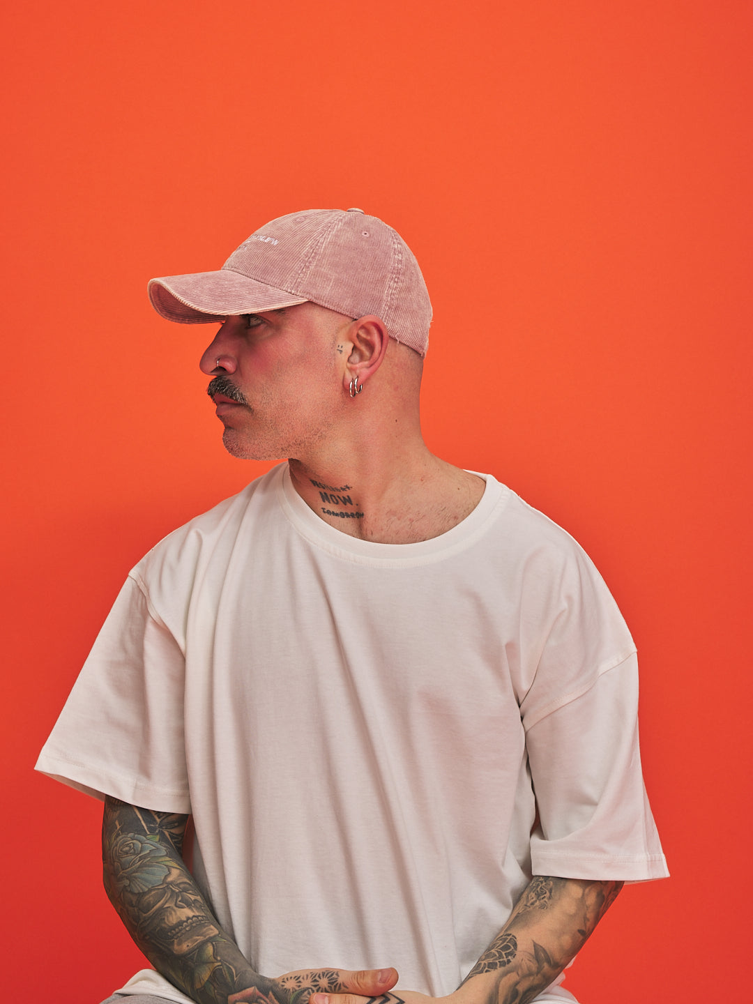 Man wearing a light pink cap and white t-shirt against an orange background