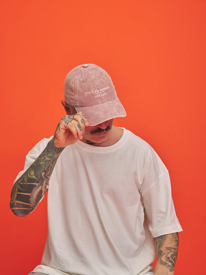 Person wearing a pink cap and white t-shirt against an orange background
