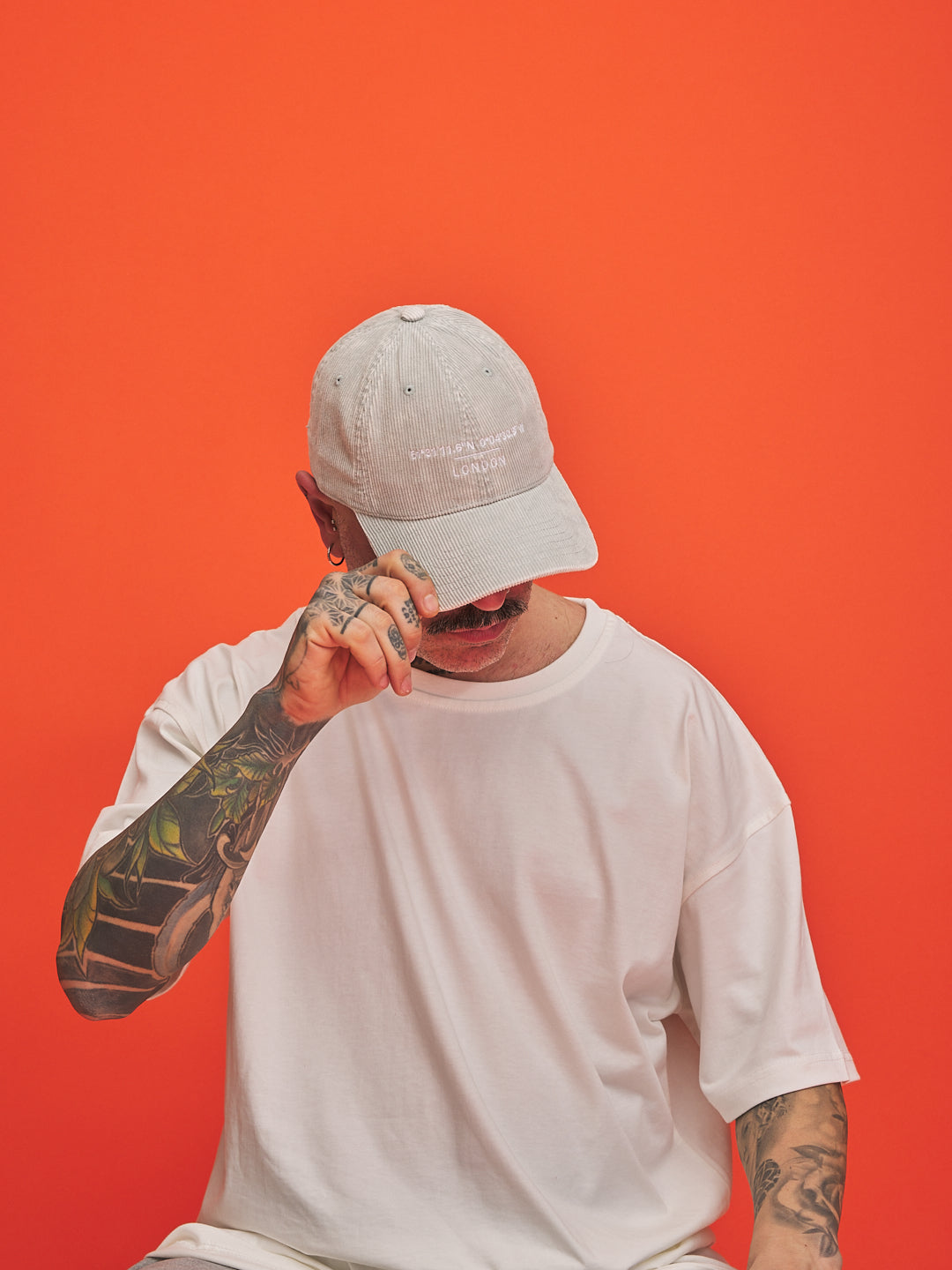 Person wearing a light gray cap and white t-shirt against an orange background