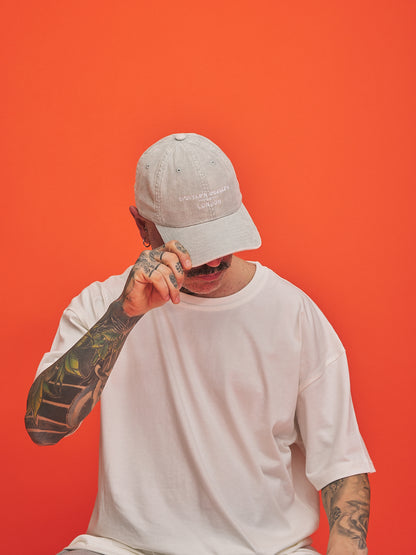 Person wearing a light gray cap and white t-shirt against an orange background