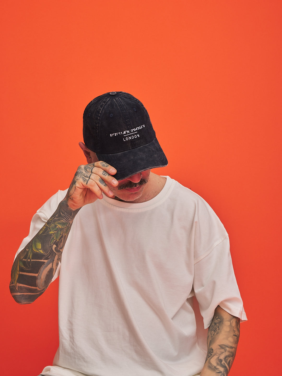 Person wearing a navy cap and white t-shirt against an orange background