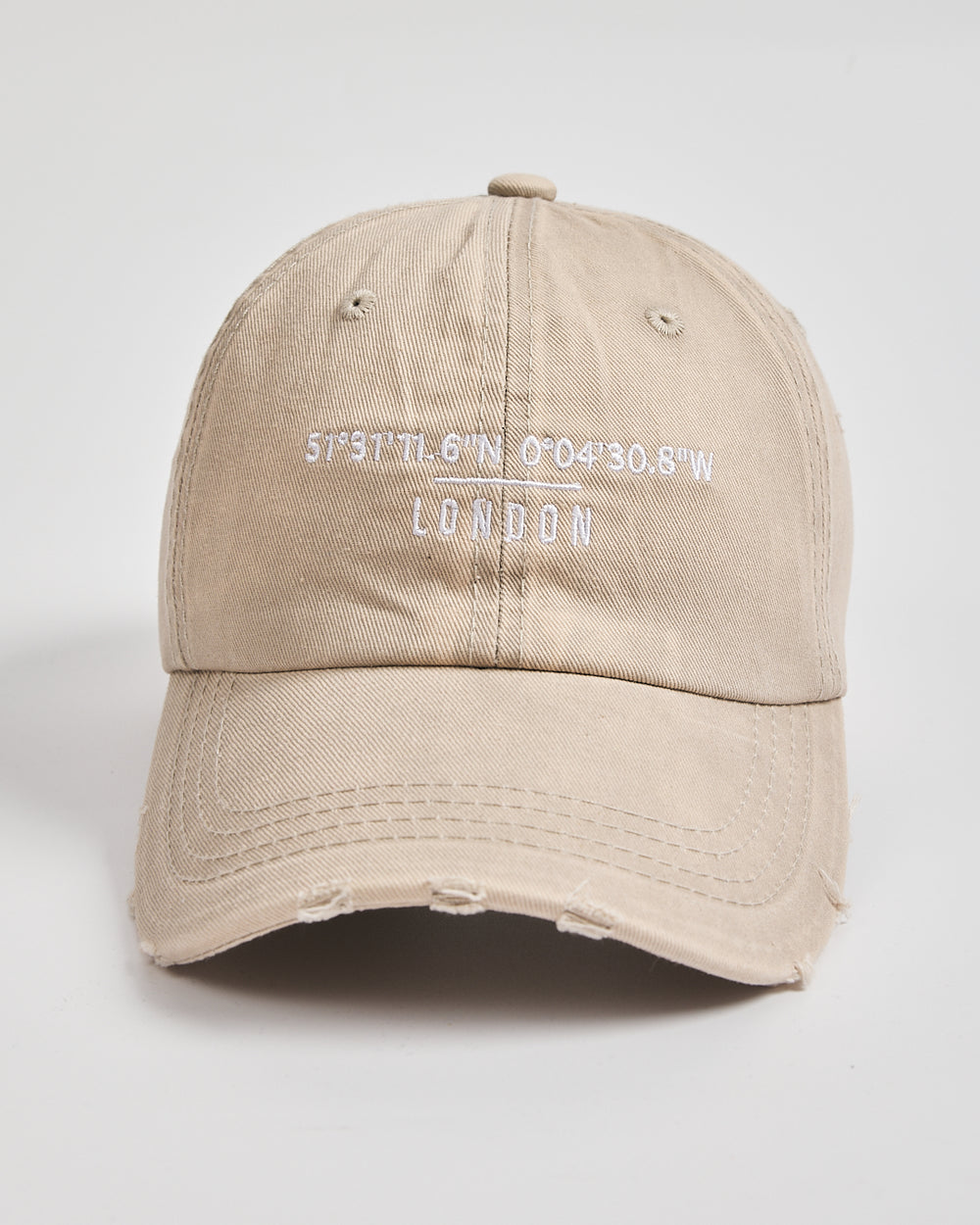 Beige cap with 'London' coordinates on a light gray background