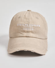 Beige cap with 'London' coordinates on a light gray background