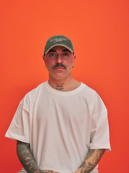 Person wearing a white t-shirt and green cap against an orange background